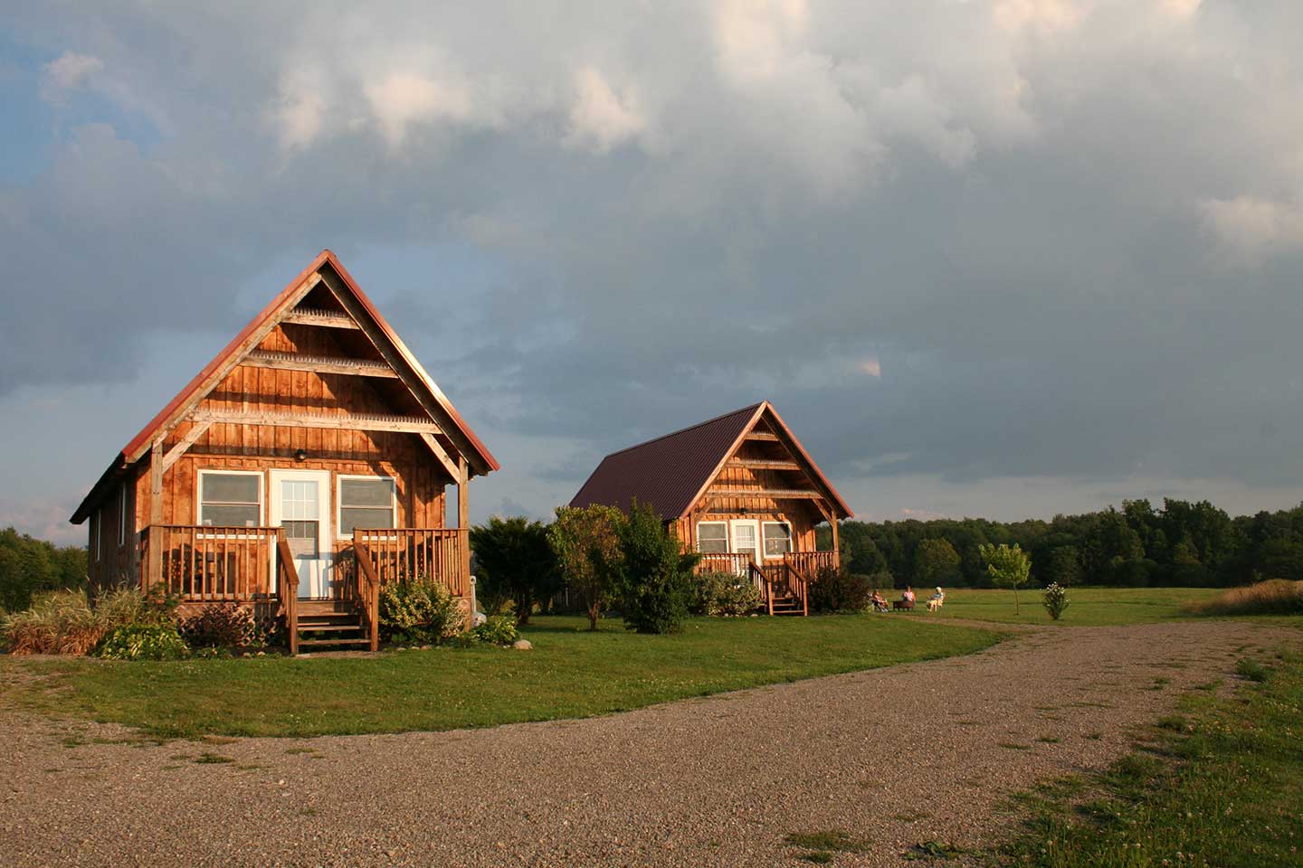 Front of cabins during a summer dusk with visitors relaxing by campfire